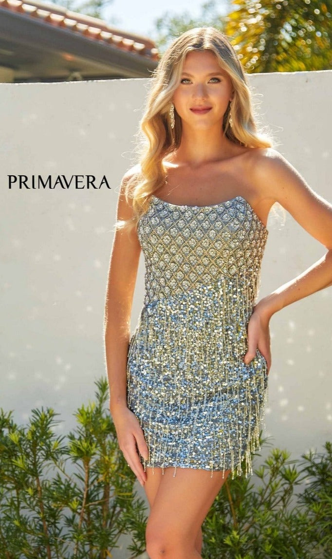 A woman in the Strapless Fringe Hoco Dress: Primavera 4229 with a sequin-print bodice stands outdoors in sunlight, greenery, and a white wall behind her.